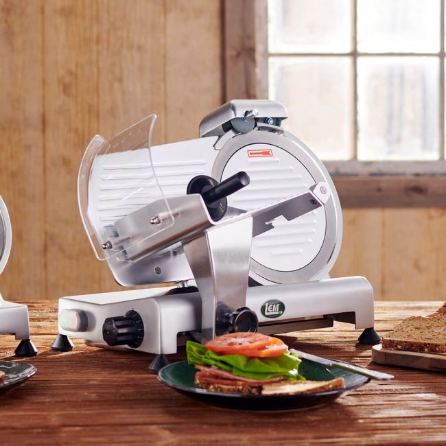 A picture of freshly sliced meat on a sandwich on a wooden table with a meat slicer