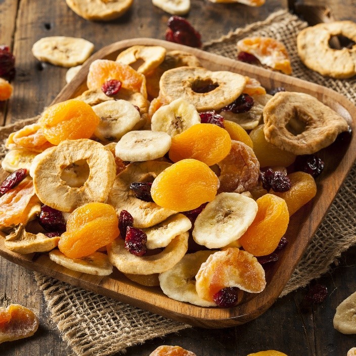 dried fruits on a wooden square plate with more dried fruits scattered around a table