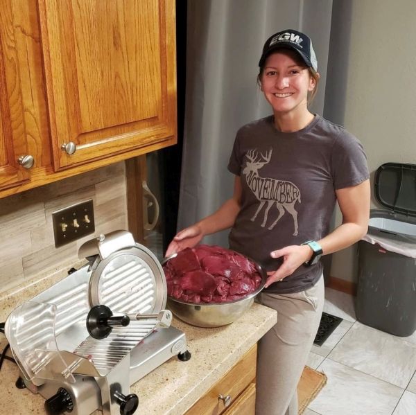 Woman holding a bowl of meat next to a meat slicer