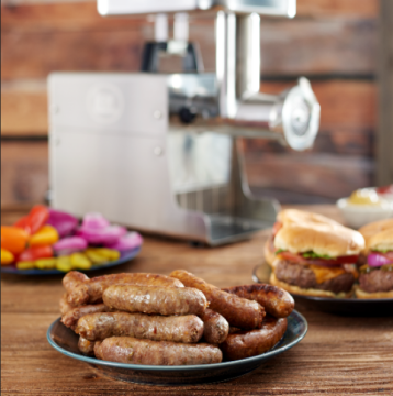 Plate of sausages and burgers on table with a meat grinder